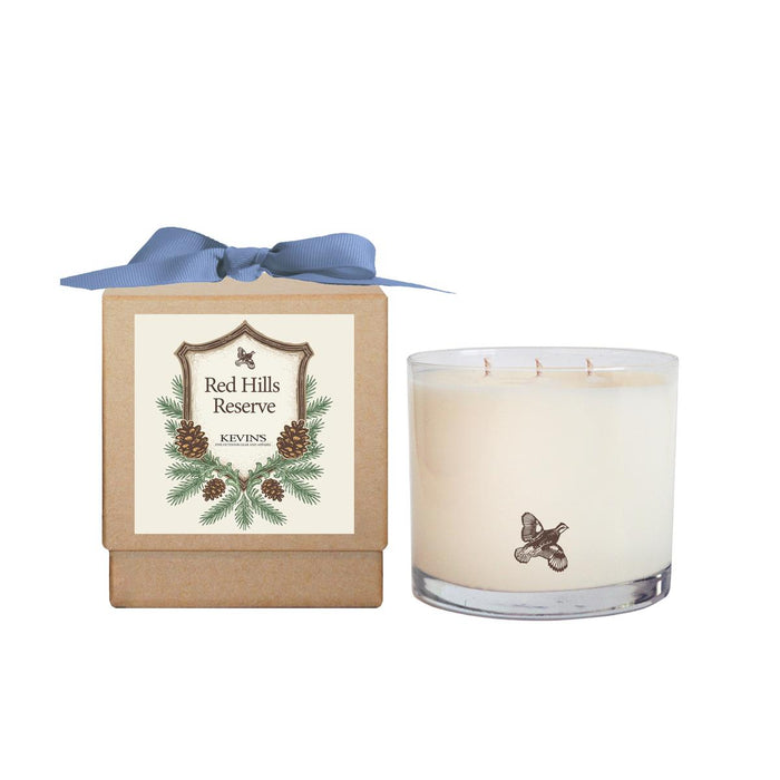 Kevin’s Red Hills Reserve 30oz three-wick soy candle in a glass jar next to a kraft gift box with a blue ribbon.
