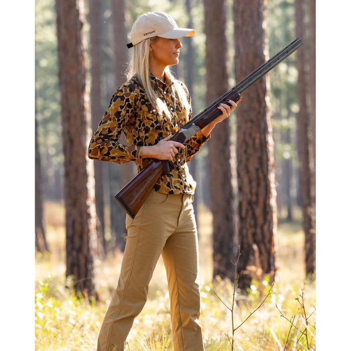 Woman wearing tan performance brush pants with a flattering, tailored fit in a wooded field setting.