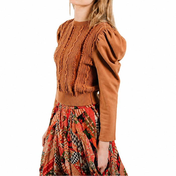 Caramel knit pullover with sculpted puff sleeves, cable-knit detailing, and a ribbed hem worn with a patterned skirt.