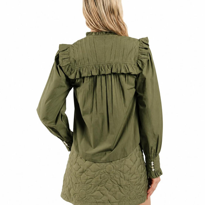 Olive green blouse with pleated yoke, ruffle trim, and buttoned cuffs worn with a quilted floral skirt.