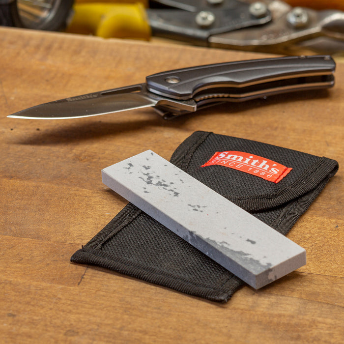 Smith's 4-inch Soft Arkansas sharpening stone on a black fabric pouch with a pocket knife on a wooden workbench.