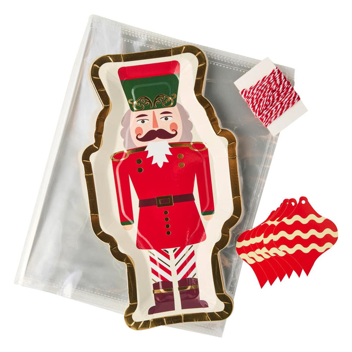 Nutcracker-shaped paper cookie tray with gold trim, clear gift bags, red and white bakers twine, and ornament-shaped gift tags.