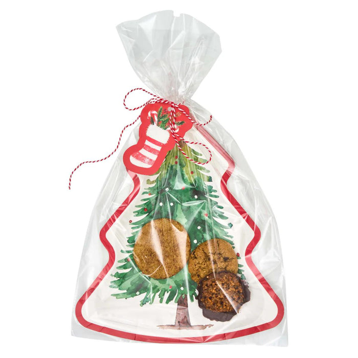 Christmas tree-shaped paper cookie tray in a clear bag with a stocking gift tag and red and white bakers twine.