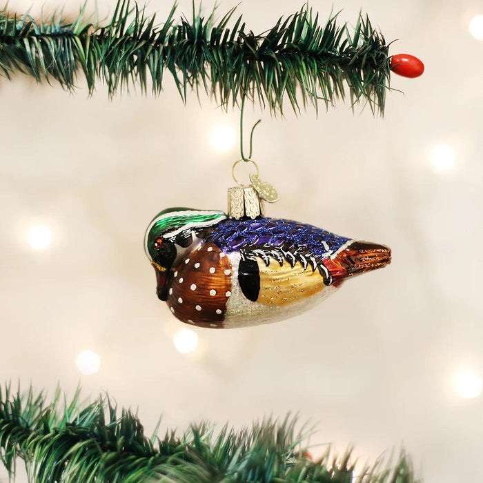 Hand-painted blown glass wood duck ornament with vibrant plumage, glitter accents, and intricate details hanging on a tree.