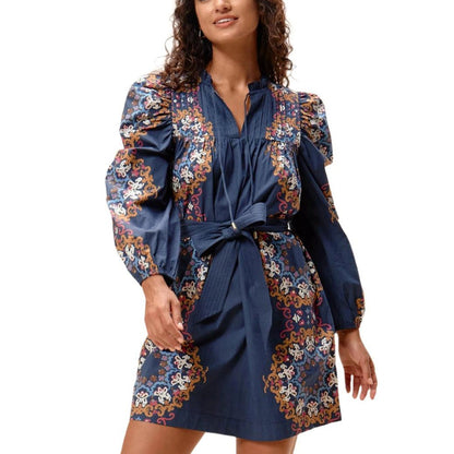 Model wearing a navy organic cotton mini dress with floral print, pintuck details, ruched sleeves, and a tie-waist sash.