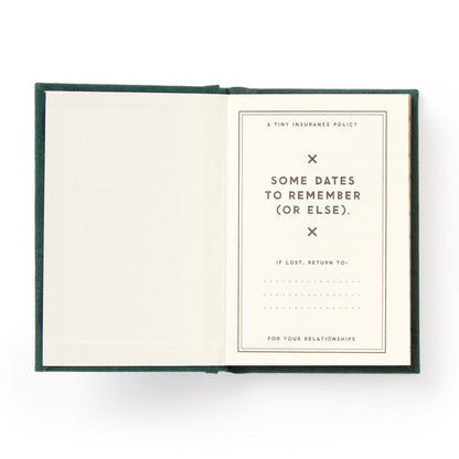 A hard-bound Brass Monkey Dates People Get Mad If I Forget Tiny Diary lies open with gilded pages: one blank, the other titled A Tiny Insurance Policy—Some Dates to Remember (Or Else), plus a spot for contact info if lost.