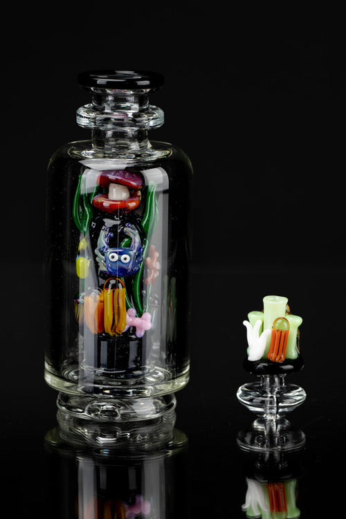 Hand-blown glass water pipe featuring colorful insect and mushroom designs, with a separate glass piece alongside, all reflected on a dark surface.
