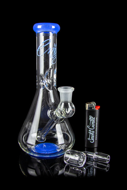 Blue glass water pipe with cannabis accessories on a reflective surface.