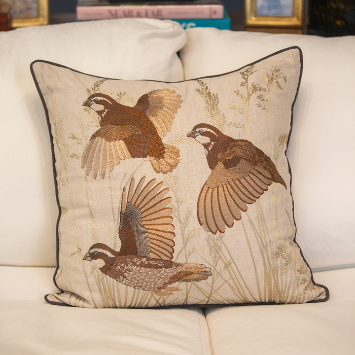 22-inch beige linen pillow cover featuring detailed embroidered flying quail motifs and a tailored dark cording border.