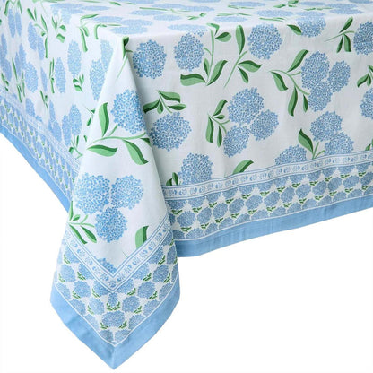 Cotton tablecloth with blue hydrangea block print and green leaves on a white background with a light blue border.