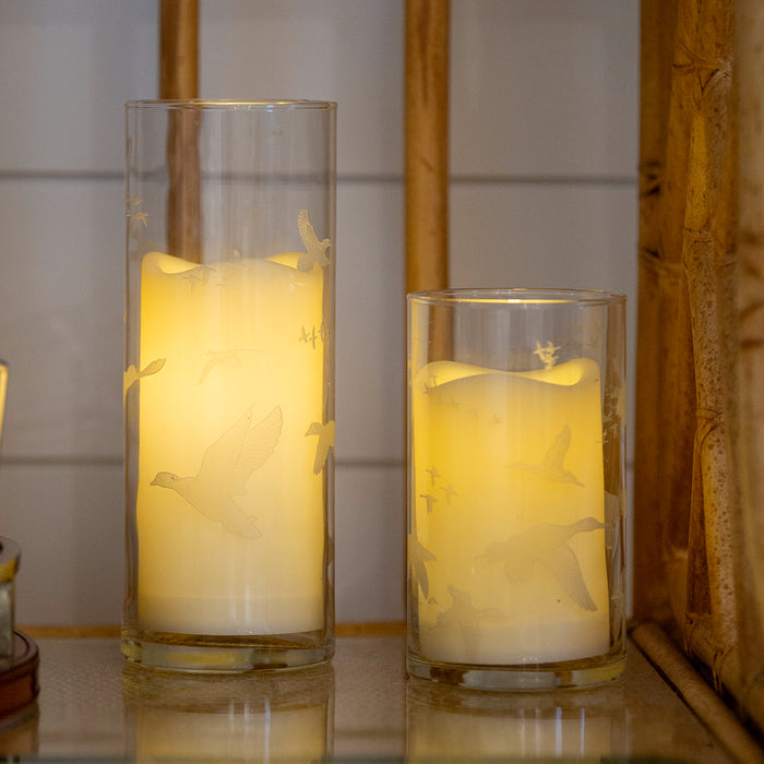 Two clear glass hurricane candle holders etched with flying quail and waterfowl silhouettes, glowing with warm LED candles.