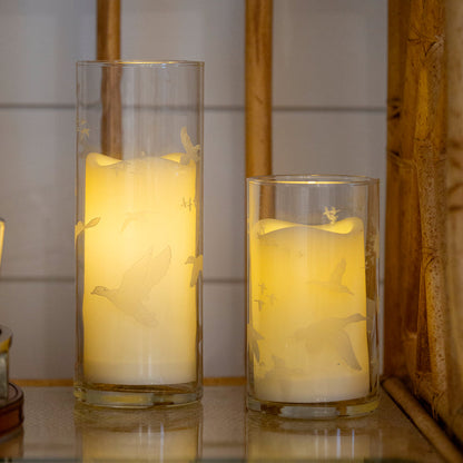 Two clear glass hurricane candle holders etched with flying quail and waterfowl silhouettes, glowing with warm LED candles.