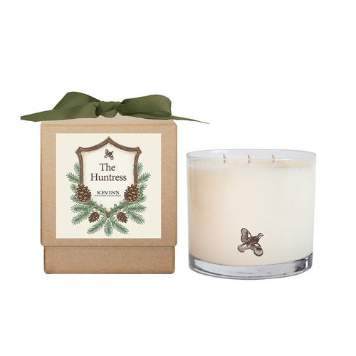 Three-wick soy candle in a glass jar with a bird logo next to a gift box with a green ribbon and pinecone label.