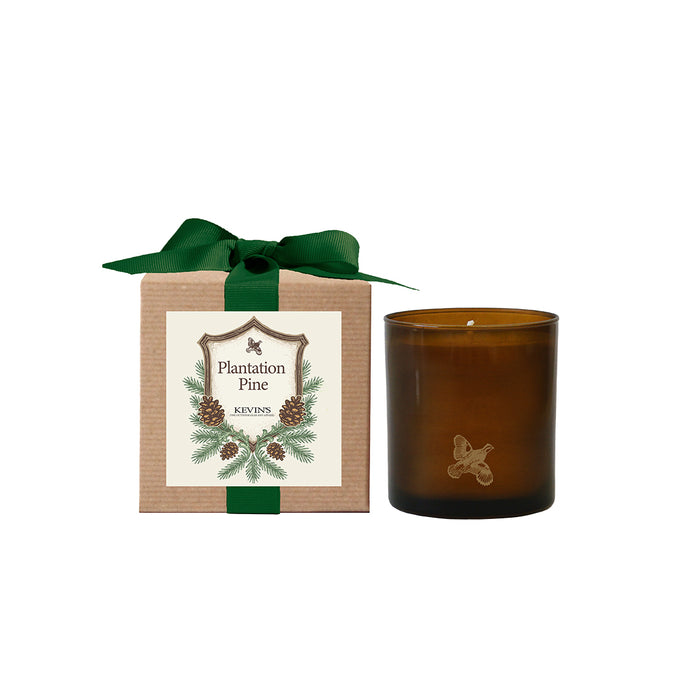 Kevin’s Plantation Pine soy candle in a brown glass jar next to a kraft gift box with a green ribbon.