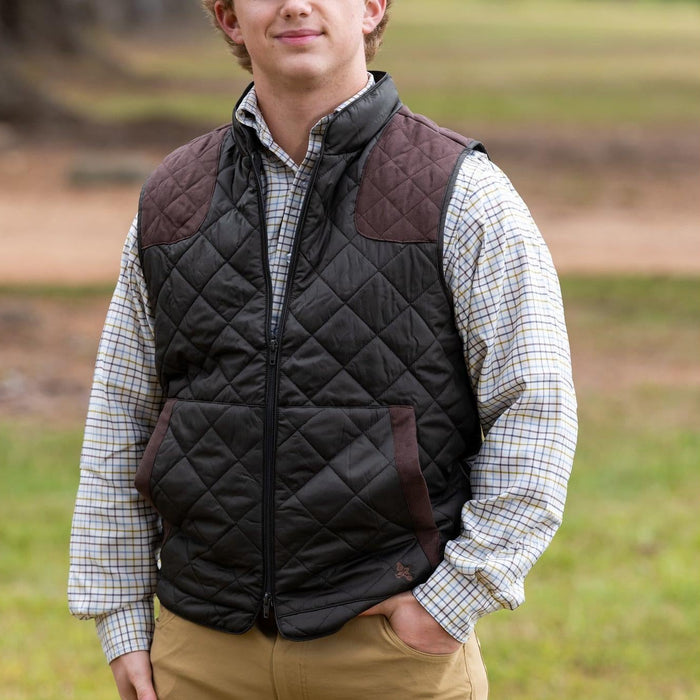 Black quilted nylon vest with brown shoulder shooting pads and a zip-front closure worn over a plaid button-down shirt.