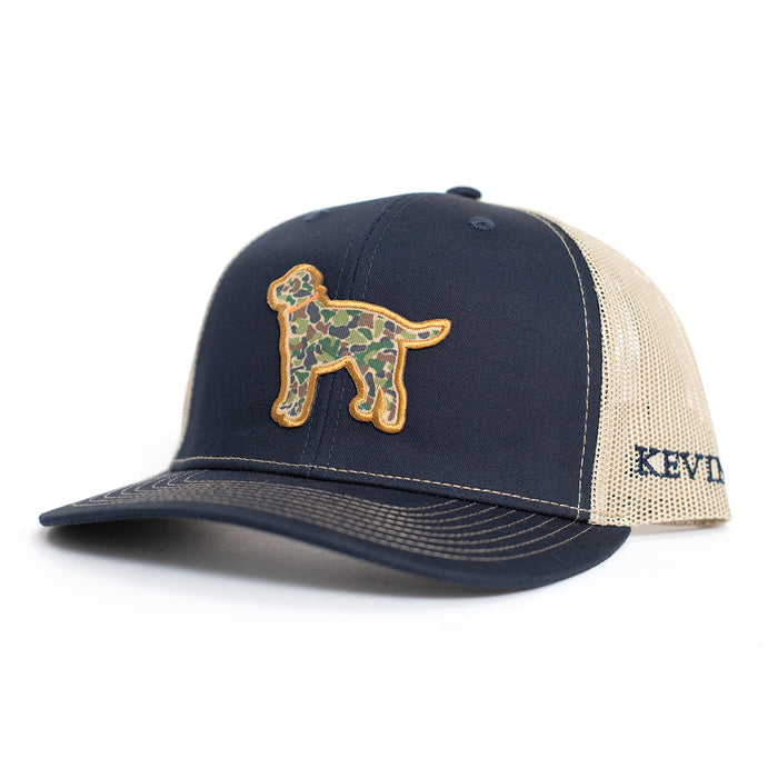 Navy blue and tan Richardson 112 trucker cap featuring a camo Labrador retriever patch and Kevin's branding.