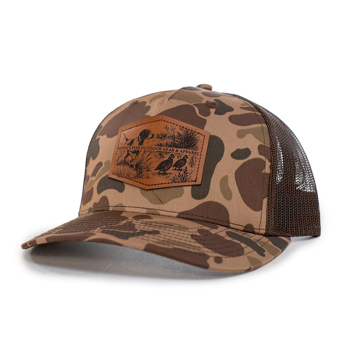 Camo Richardson 112 trucker cap with a brown leather patch featuring an embossed quail and pointer dog scene.