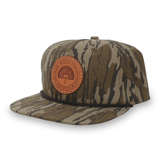 Kids' Mossy Oak camo rope cap featuring a round leather patch with a turkey fan logo and black paracord trim.