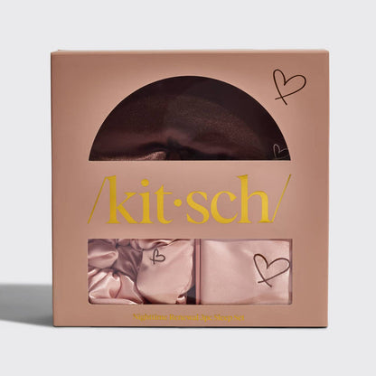 A Kitsch Nighttime Renewal 3pc Sleep Set in a pink box, displaying a satin pillowcase, scrunchie, and eye mask with heart details.