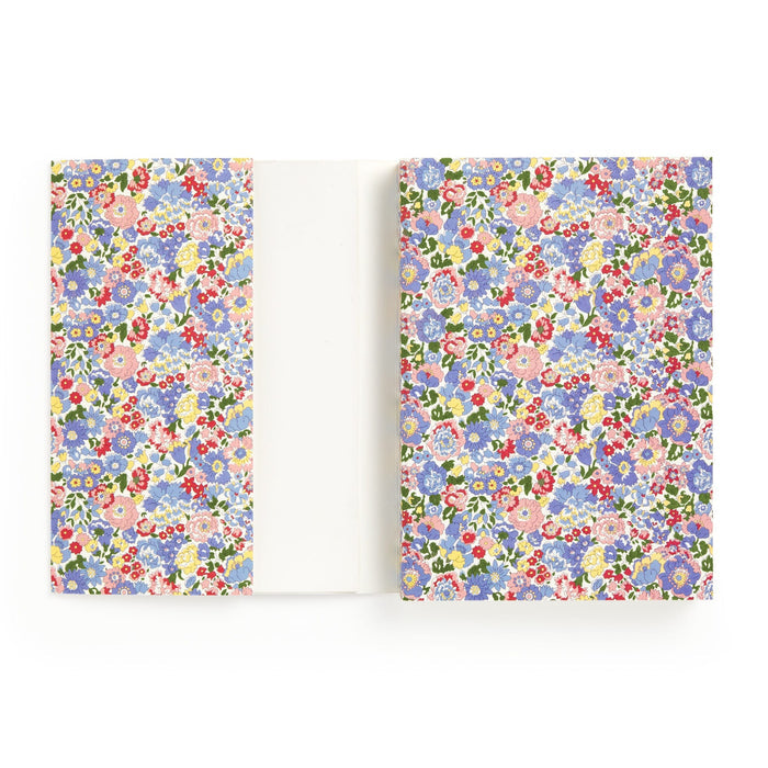 The Liberty London Liberty Nell, Annie and May Premium A5 Notebook features a white cover with colorful blue, pink, red, and purple floral patterns, inside flaps to match, and blank pages for writing or drawing.