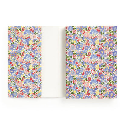 The Liberty London Liberty Nell, Annie and May Premium A5 Notebook features a white cover with colorful blue, pink, red, and purple floral patterns, inside flaps to match, and blank pages for writing or drawing.