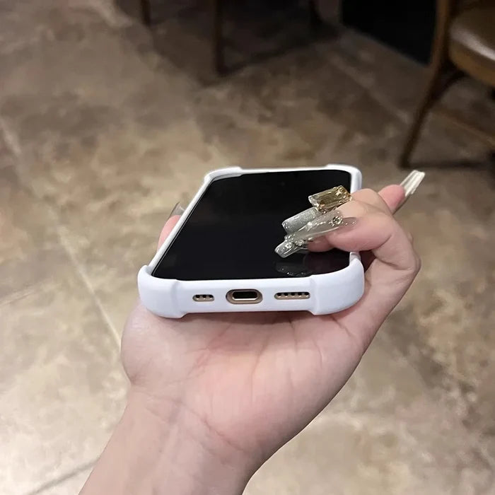White smartphone in a protective case with long, decorative fingernails holding it.