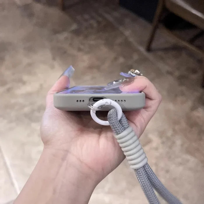 A hand holding a smartphone in a protective case with a gray braided lanyard attached.