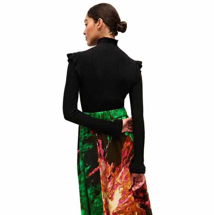 Black ribbed turtleneck sweater with ruffled shoulders and cuffs, worn with a vibrant green and floral print skirt.