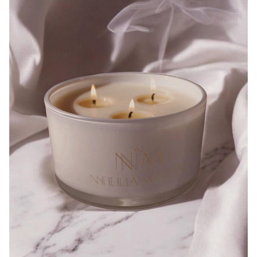 Nellamoon 22 oz soy candle in a creamy white glass jar with three lit cotton wicks on a marble surface.
