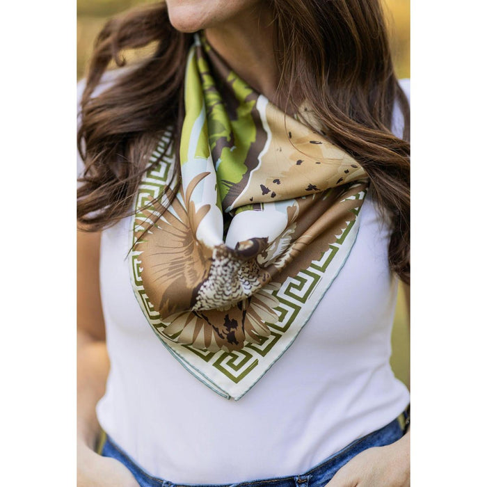 Woman wearing a silk twill scarf featuring an English pointer, quail, and Greek key border in navy, ochre, and cream tones.