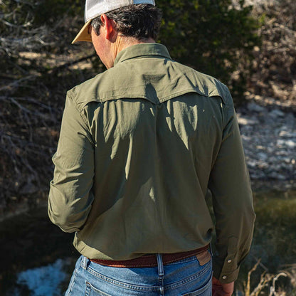 Olive green Poncho Brazos western long sleeve shirt with a vented back, worn outdoors with jeans and a trucker hat.
