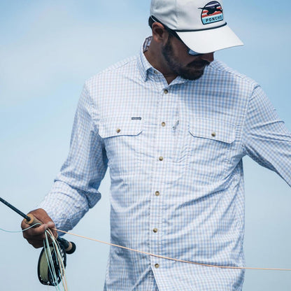 Man wearing a light blue and white gingham long-sleeve performance fishing shirt with chest pockets and a matching logo cap.