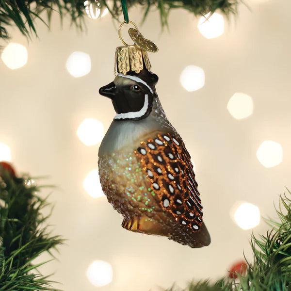Hand-painted blown glass quail ornament with glittered brown and white plumage hanging on a Christmas tree.
