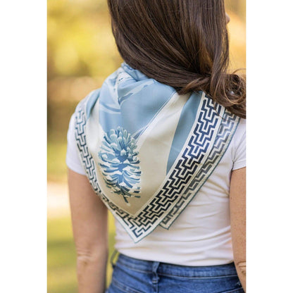 Blue silk twill scarf featuring a pinecone border and geometric patterns worn around the neck of a woman.