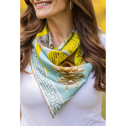 Woman wearing a blue and yellow silk twill scarf featuring quail, geometric patterns, and pinecone borders.