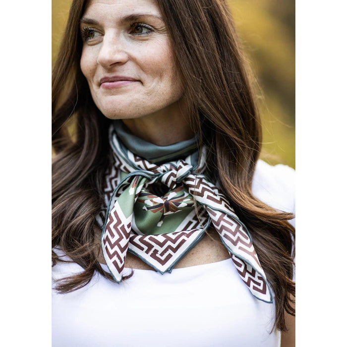 Woman wearing a blue and brown silk twill scarf featuring bobwhite quail and geometric patterns tied around her neck.