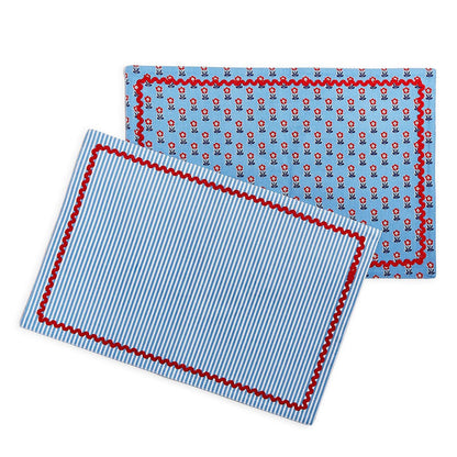 Reversible cotton placemats with blue floral print and blue striped pattern, finished with a red scalloped trim.