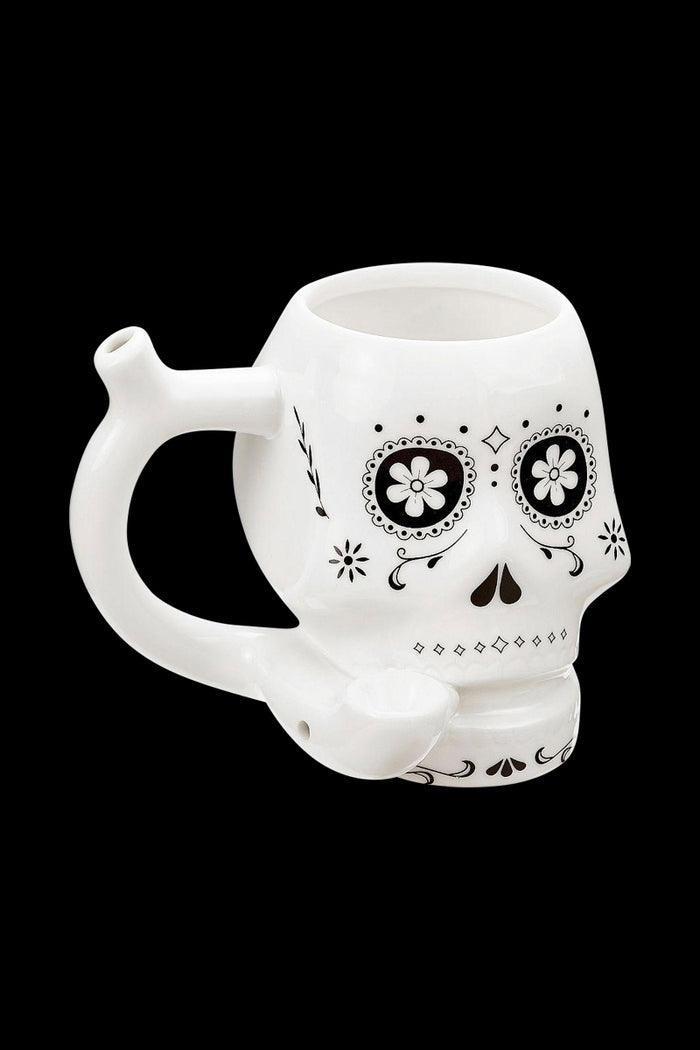 Three-quarter view of the Roast & Toast "Sugar Skull" Ceramic Pipe Mug showing the white skull-shaped mug with black floral eye designs and a curved pipe handle against a black background