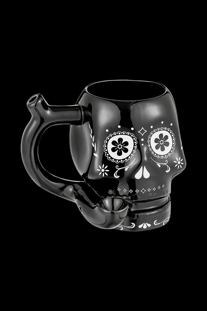 Three-quarter view of the Roast & Toast "Sugar Skull" Ceramic Pipe Mug in glossy black with white sugar-skull floral face art and a pipe-style handle.