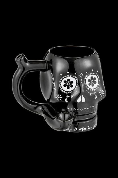 Three-quarter view of the Roast & Toast "Sugar Skull" Ceramic Pipe Mug in glossy black with white sugar-skull floral face art and a pipe-style handle.