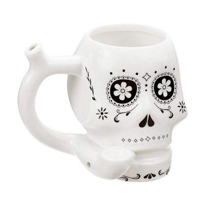 Three-quarter view of the Roast & Toast "Sugar Skull" Ceramic Pipe Mug showing its white skull shape, black floral eye designs, side handle stem, and front bowl.