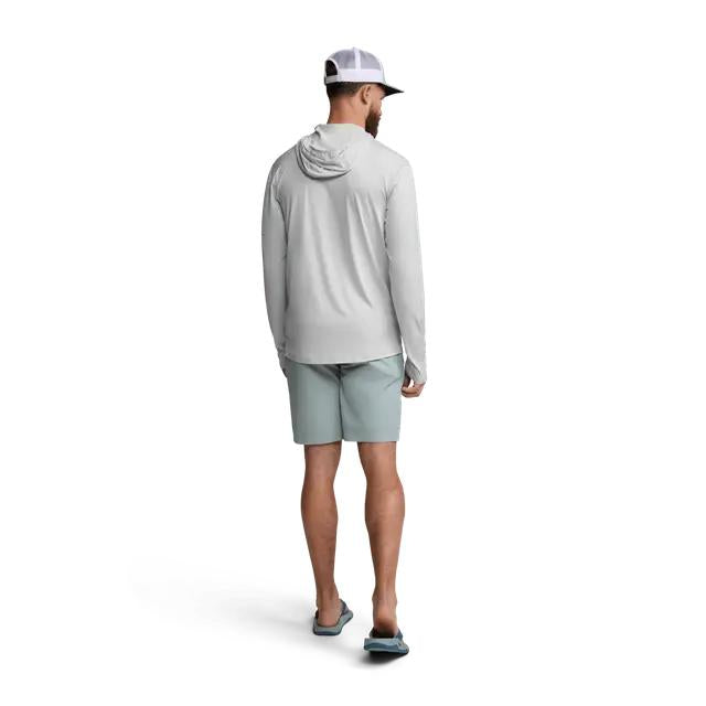 Man wearing a light grey Sitka Guard Sun Hoodie with a hood, long sleeves, and thumb loops, paired with light green shorts.