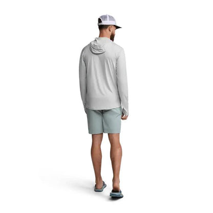 Man wearing a light grey Sitka Guard Sun Hoodie with a hood, long sleeves, and thumb loops, paired with light green shorts.