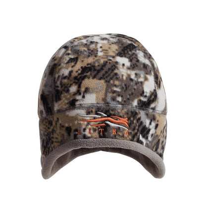 Sitka Stratus windproof micro-fleece hunting beanie in camo print with acoustic ear ports and orange logo.