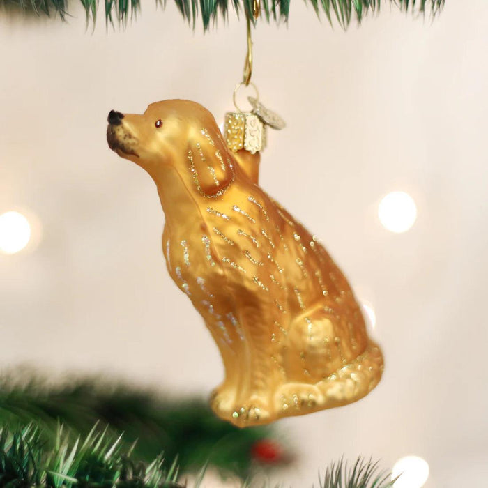 Hand-painted, glittered golden glass ornament shaped like a sitting Golden Retriever, hanging on a Christmas tree.