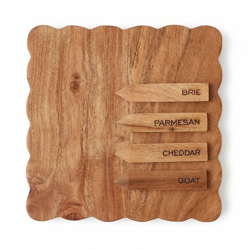Square acacia wood cheese board with scalloped edges and four labeled wooden cheese markers.