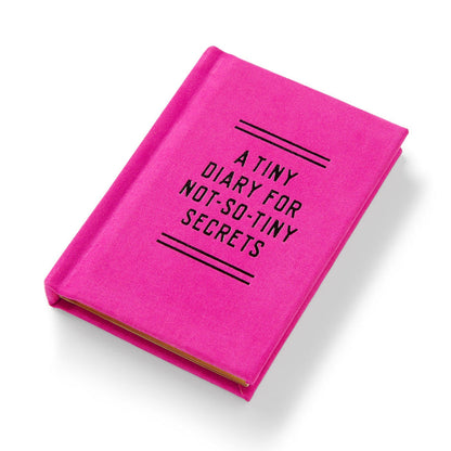 The Brass Monkey Tiny Diary for Not So Tiny Secrets is a small, bright pink diary with black cover text and gold-edged pages, shown closed on a white background.