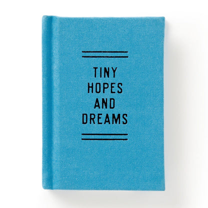 The Brass Monkey Tiny Hopes and Dreams Tiny Diary is a small, blue hardbound notebook with Tiny Hopes and Dreams in black on the cover, along with decorative lines. Photographed against a white background.
