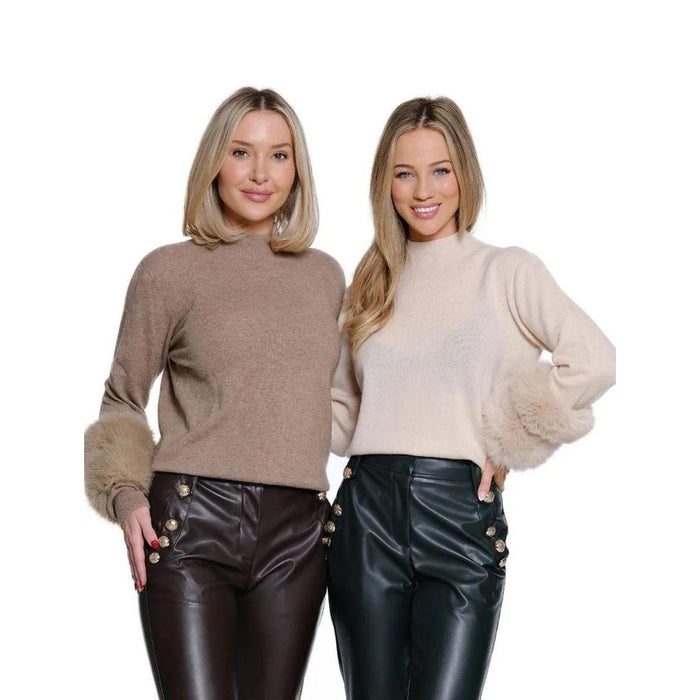 Two women wearing sleek leather-like pants with gold side buttons, paired with cozy mock-neck sweaters featuring faux fur cuffs.