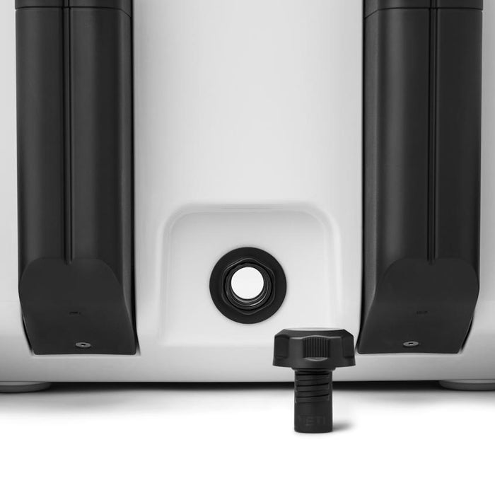 Black YETI BestDam leakproof drain plug removed from a white Roadie cooler, showing the threaded opening and screw-cap.